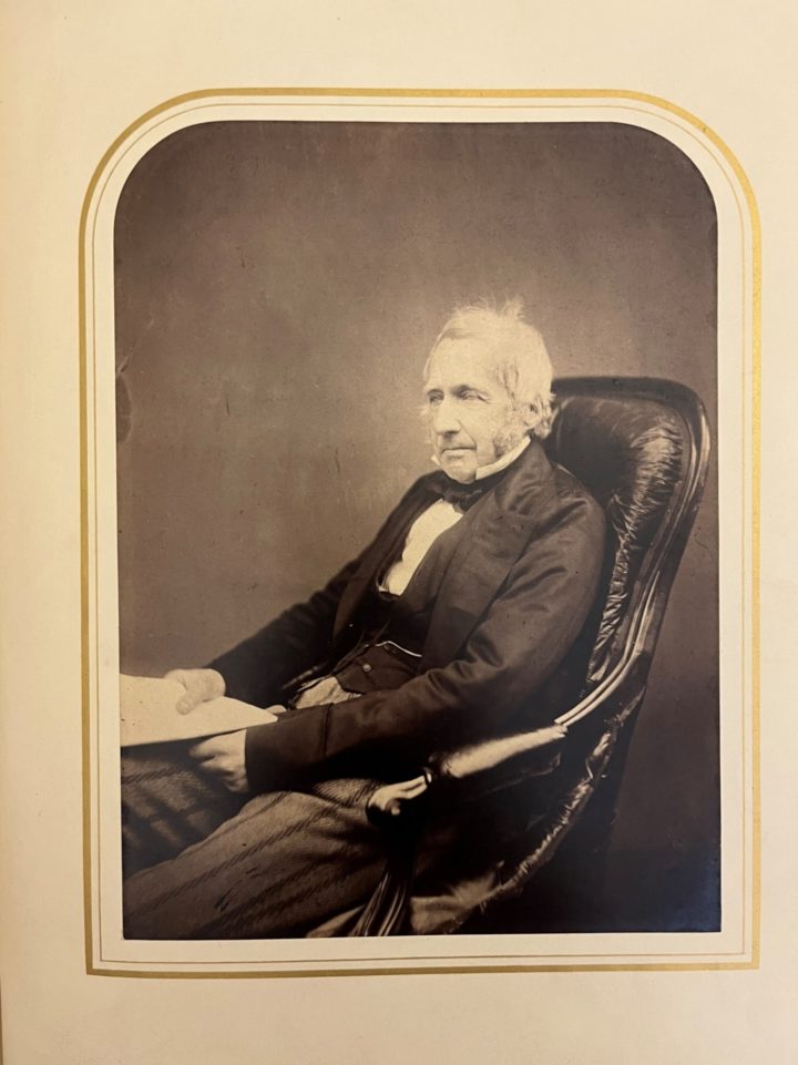 Black and white photograph of an elderly man sitting in a chair holding a document