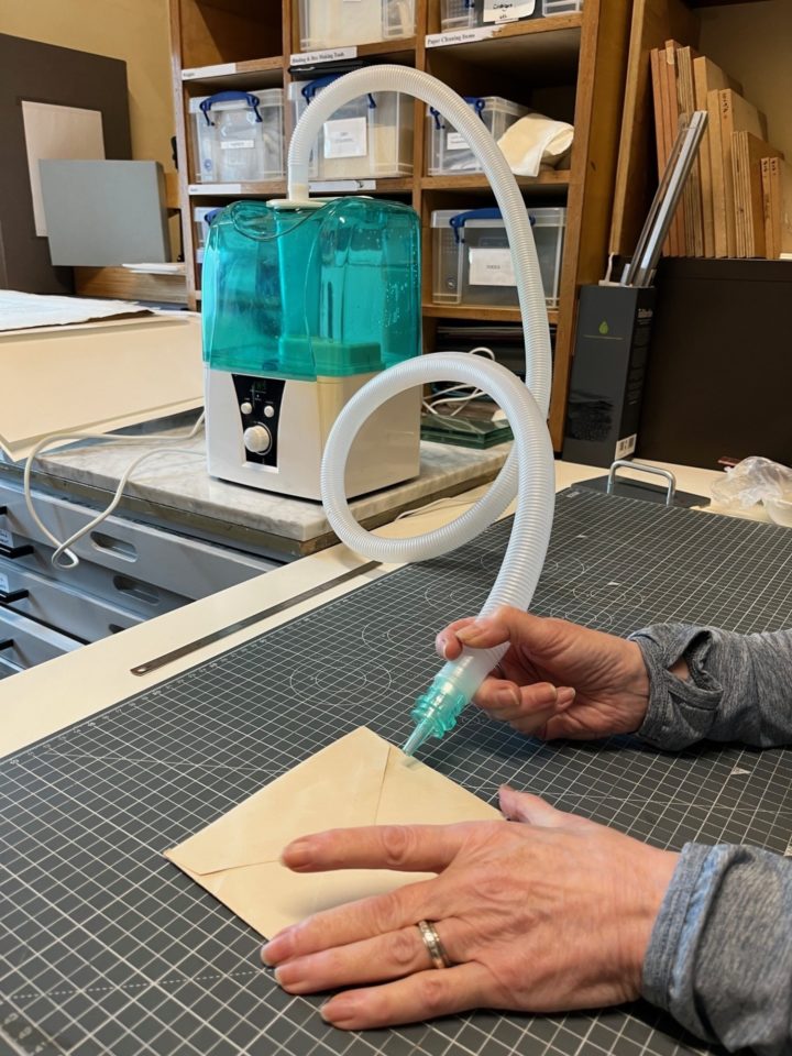 The conservator uses a nozzle to direct damp air at the seal edge of an envelope