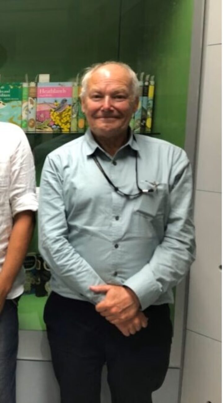 An older man in a light blue shirt with his arms crossed in front of him