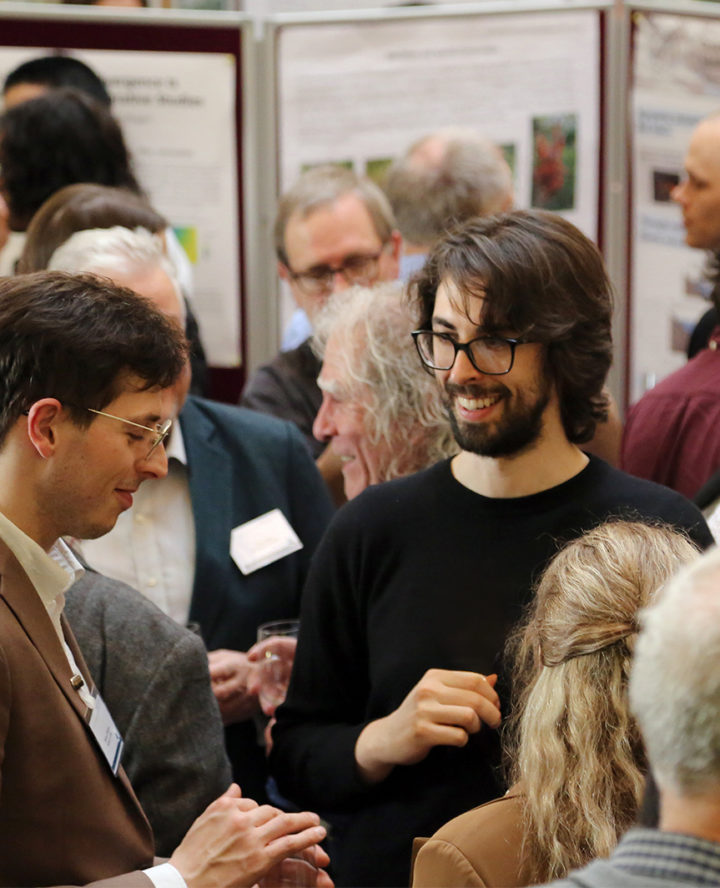 a group of event attendees talking. In the background are sceitnific posters.