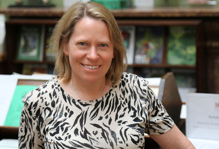 A woman with blonde hair smiles as she stands in a library