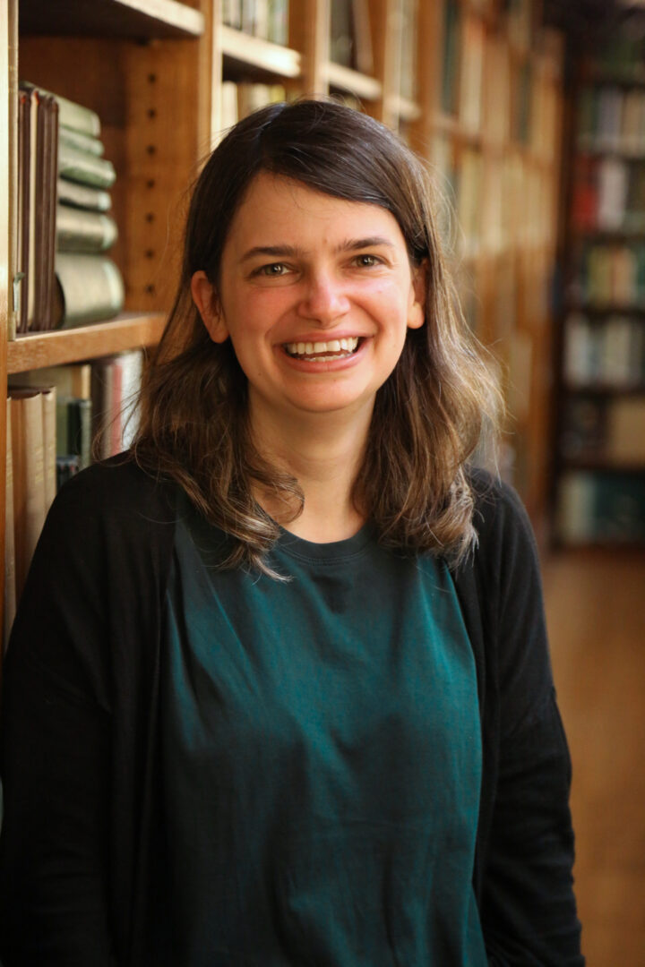 Becky smiles at the camera wearing a blue t-shirt and black cardigan.
