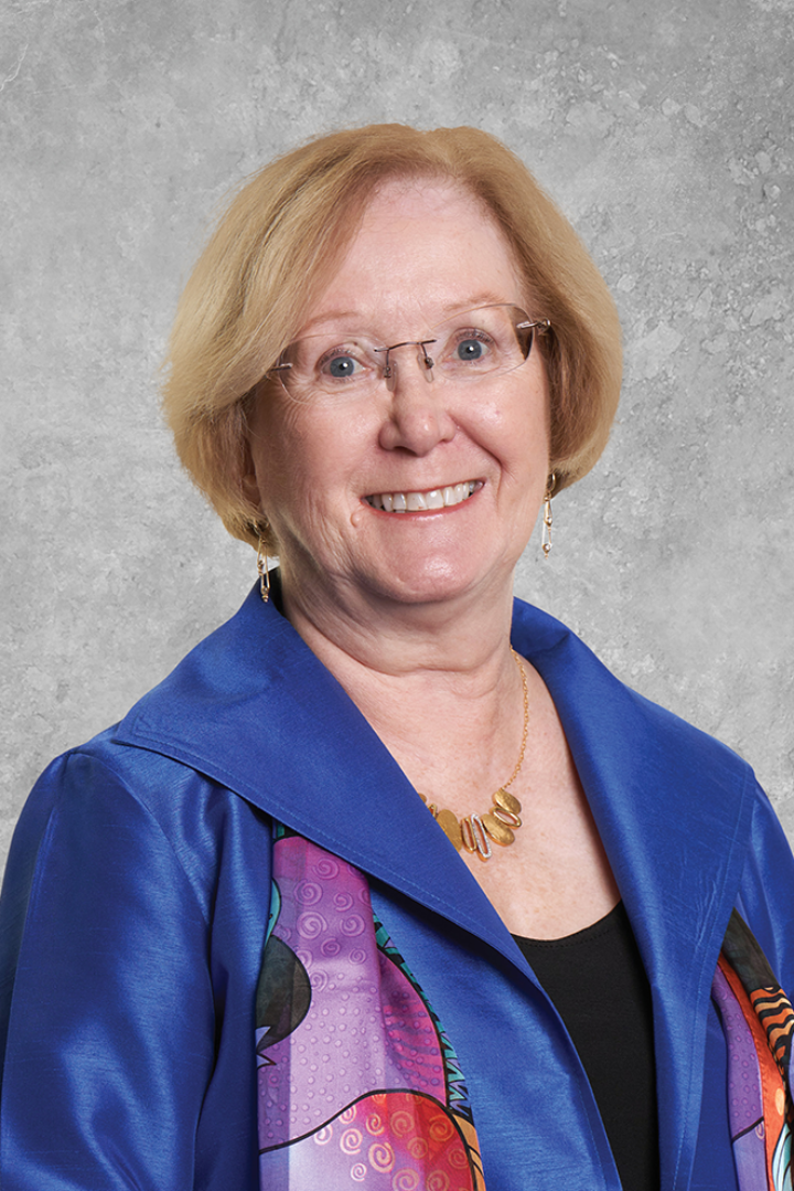 Woman with short blond bob, glasses and bright pink and purple scarf smiles at viewer