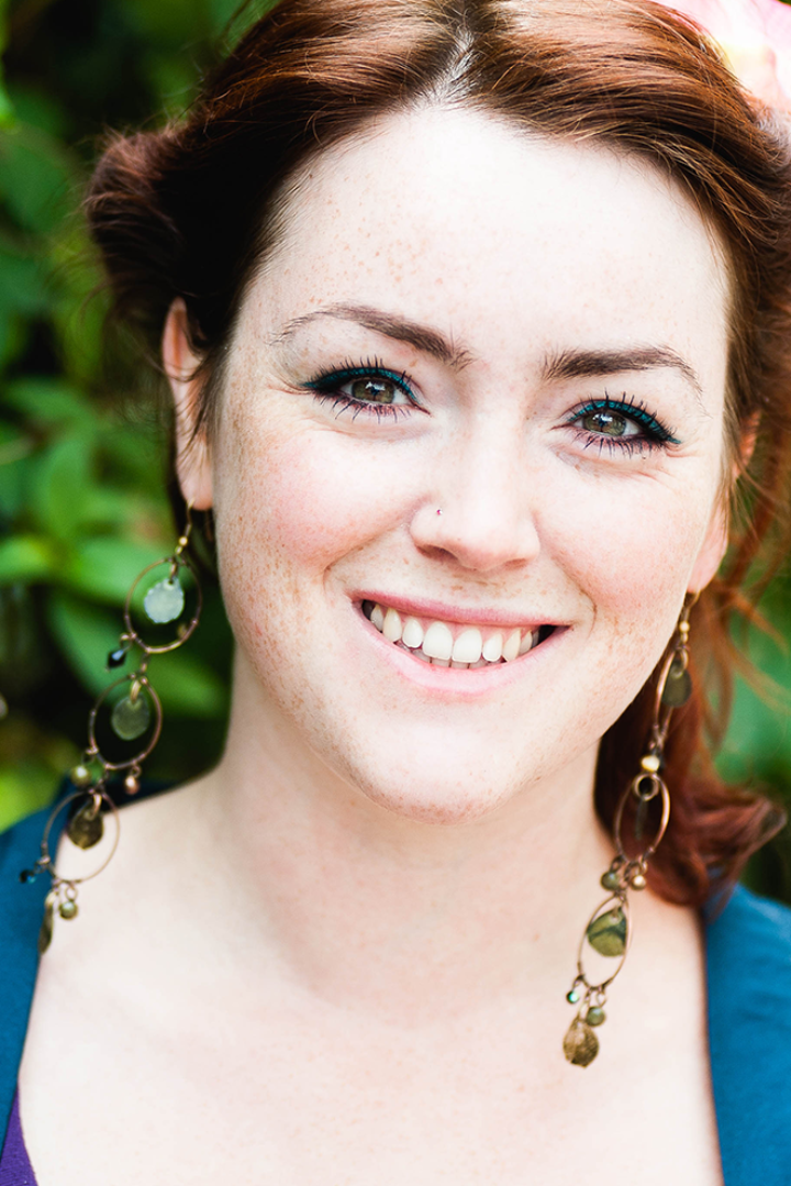 Red-haired young woman in peacock blue top smiles at the camera