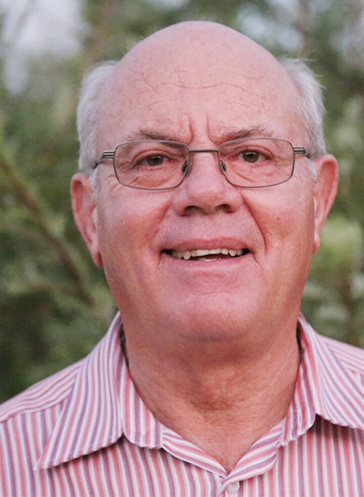 A man with glasses wearing a striped shirt smiles in the light of the setting sun