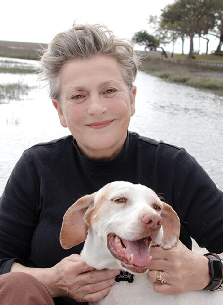 A lady with short hair sits smiling in a snowy landscape holding a happy white and brown dog