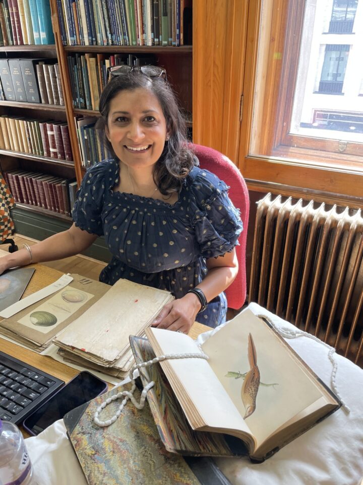An image of a young woman sat at a desk, surrounded by archival documents