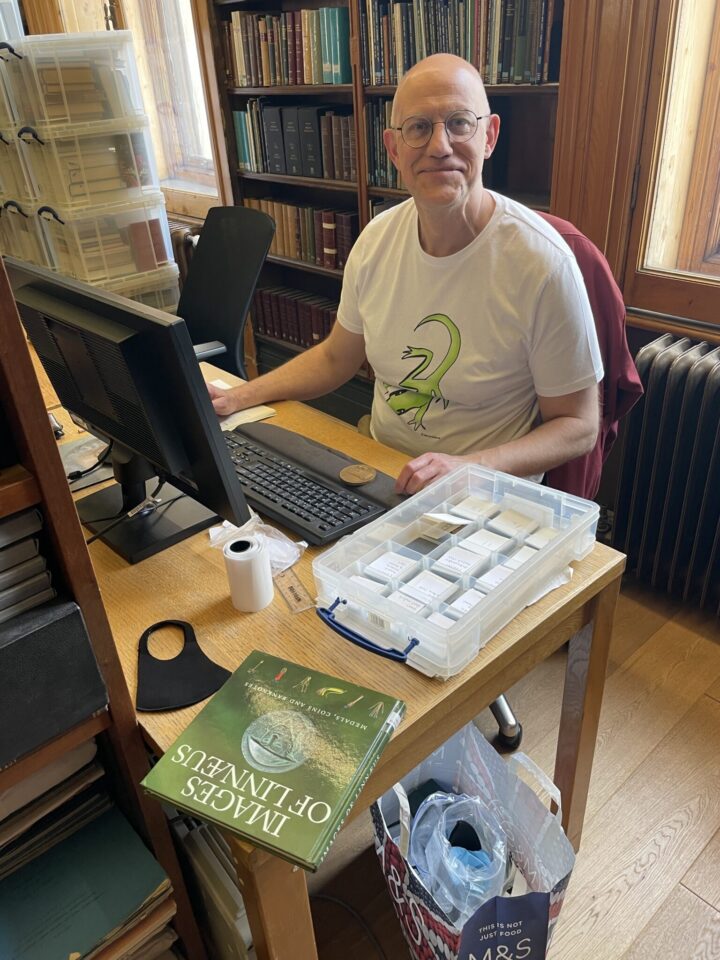 A man sat at a computer, with a box of historic medals next to him.
