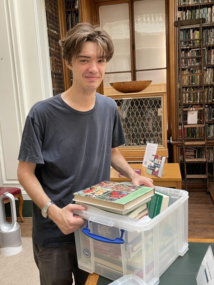 A young man holding a case of books in a library.