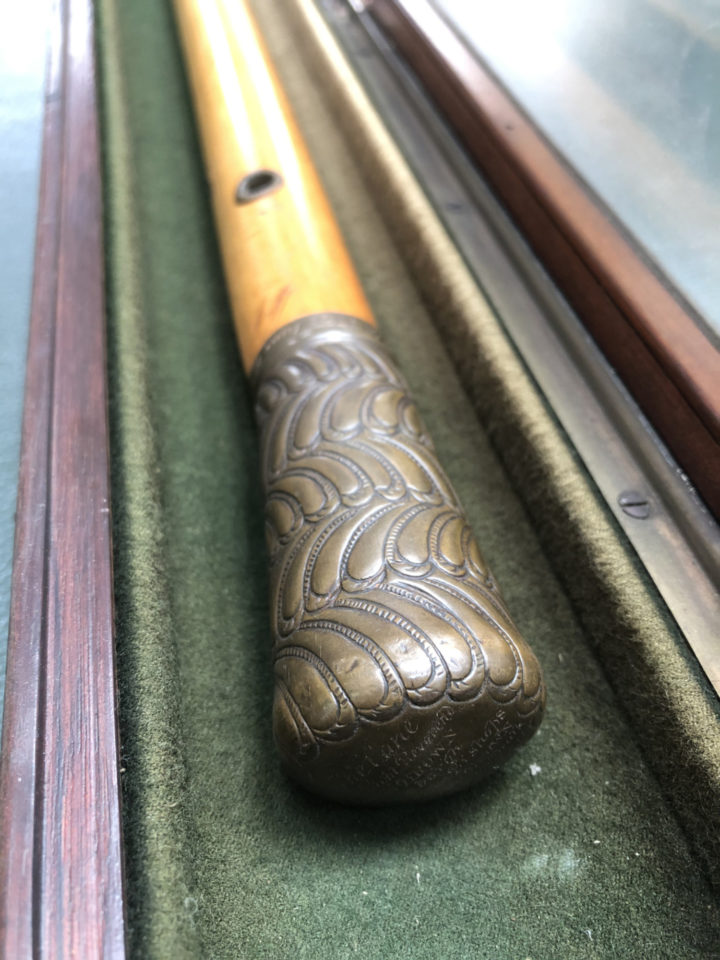 A closeup shot of the decorative handle of the cane displayed in its wooden case.