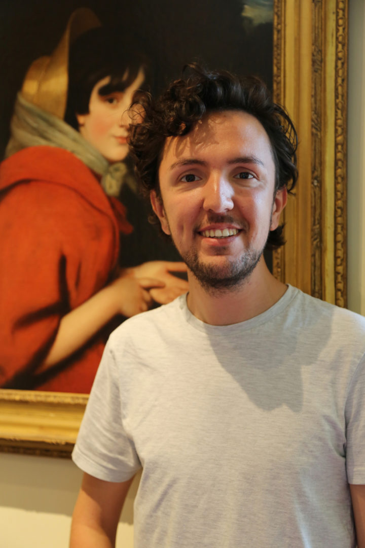 A portait photograph of Joe Burton, Education Manager at the Linnean Society, stood in front of a portrait of Pleasance Smith