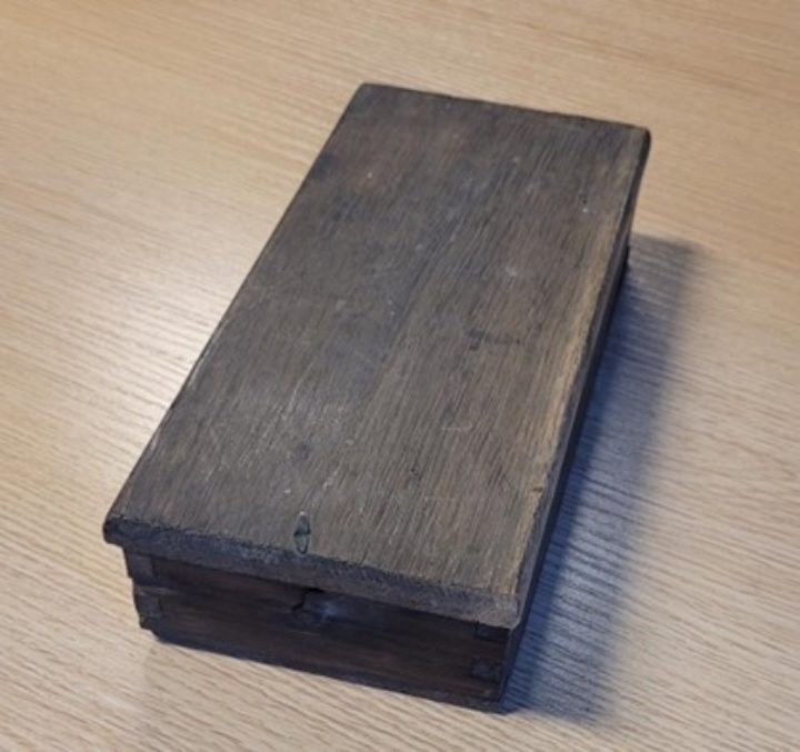 Small, closed, wooden rectangular box with metal clasp.