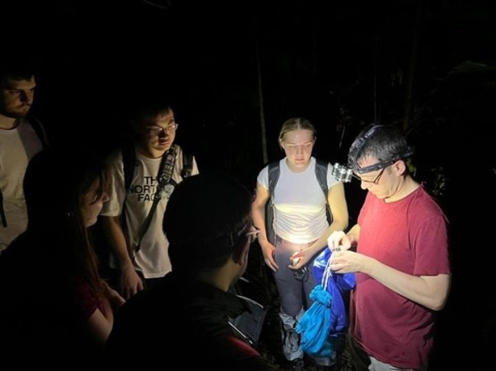 Students gather around a professor to watch wild bats be caught and weighed using blackout bags.