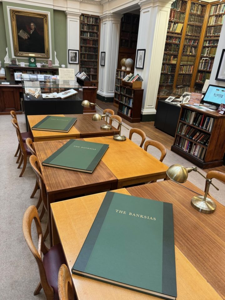 Three very large books lying flat on tables in a grand library