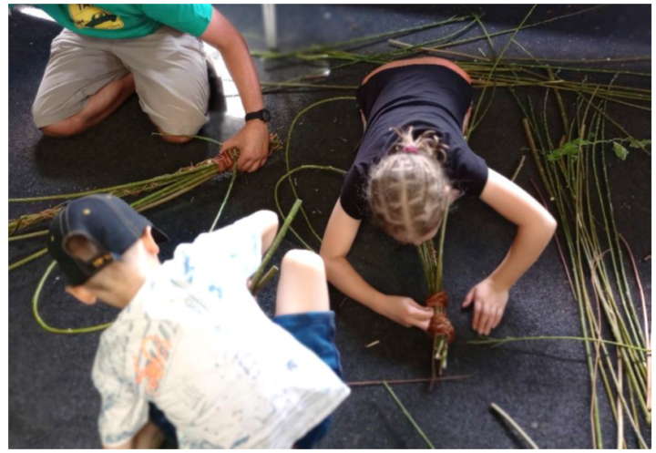 Two children working on a project with sticks and reeds