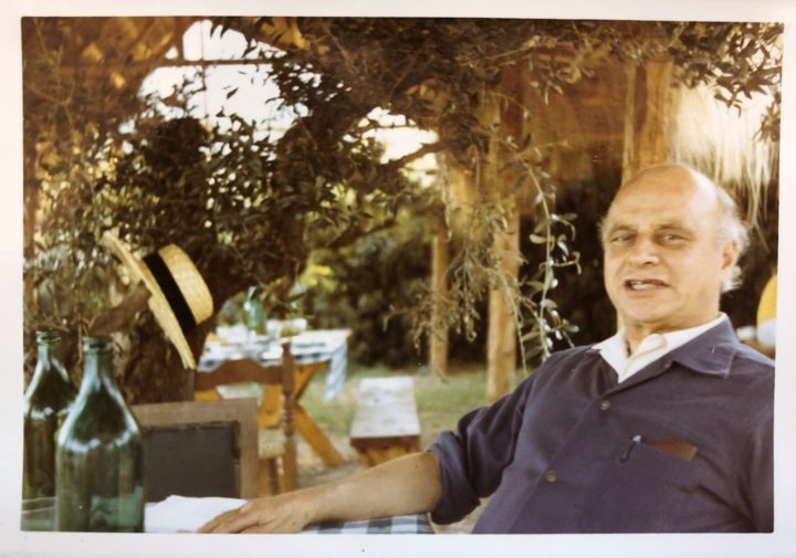 Photograph of Max Nicholson, an older white male, sitting in a garden mid conversation facing the camera around an outdoor table